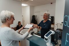 Eine Mitarbeiterin übergibt ein Protokoll an eine Patientin - Taveo - Empfang - Riga-Ring Soest